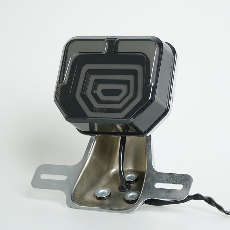 Square motorcycle LED tail light, smoked black lens with concentric geometric pattern, chrome license plate bracket, side view